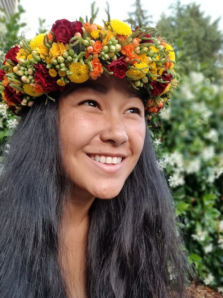 'Anakē Kalei is wearing a haku lei, while looking off into the distance and smiling